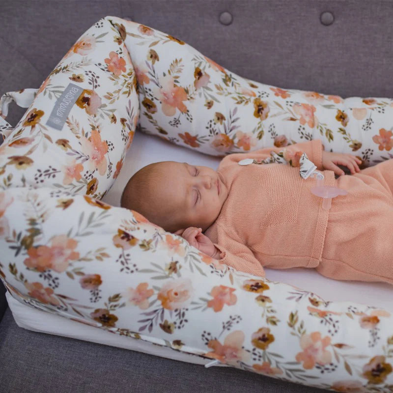 Un bebé duerme pacíficamente sobre un cojín para bebés con estampado floral. El cojín es de colores suaves y rodea al bebé, proporcionándole comodidad.